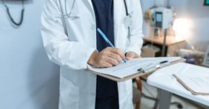 Médico de jaleco branco escreve em prancheta em consultório