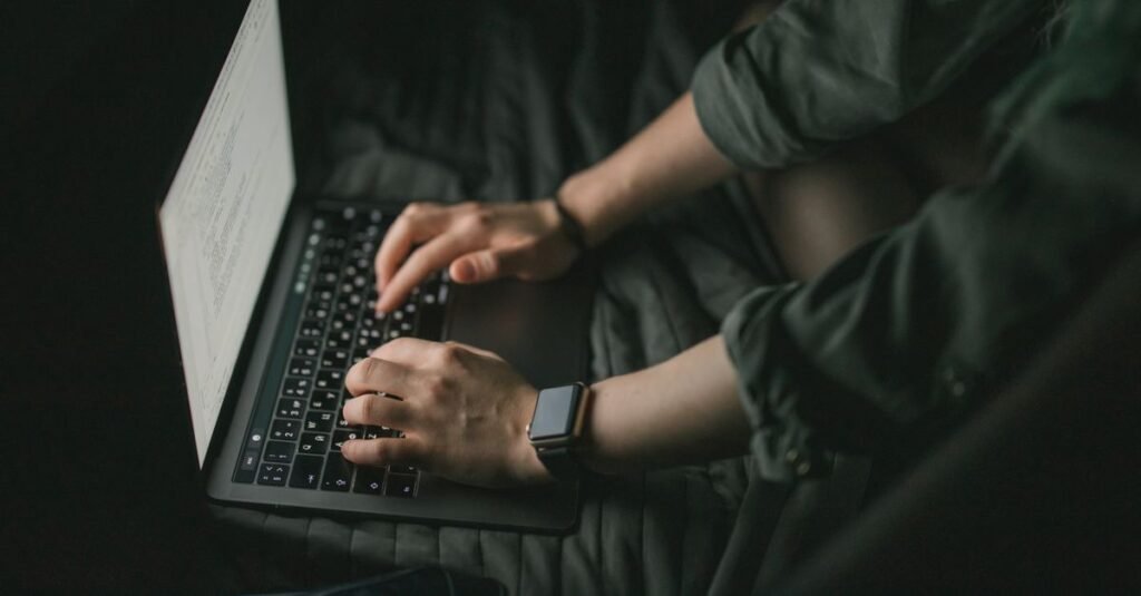 Maos digitam em notebook em ambiente escuro