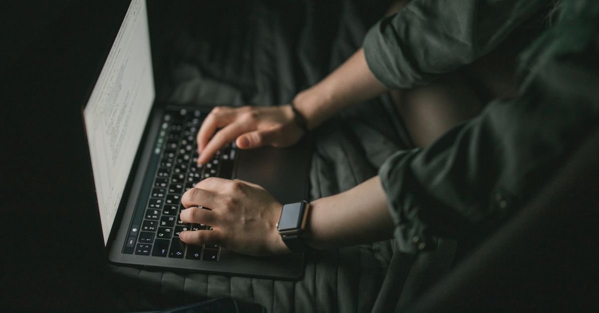 Maos digitam em notebook em ambiente escuro