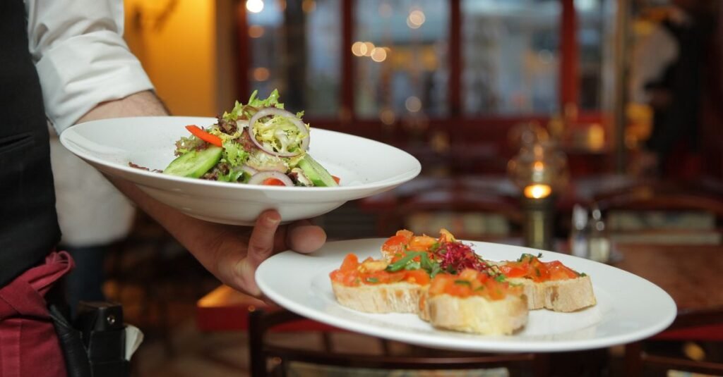 Garçom carrega dois pratos com salada e bruschetta em restaurante