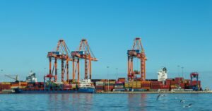 Guindastes e navios movimentam contêineres em porto