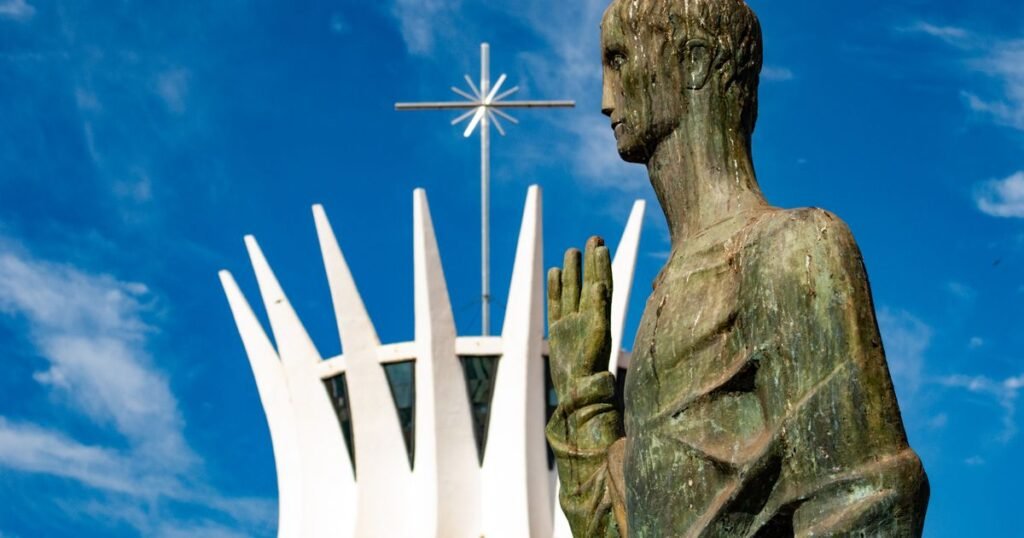 Catedral de Brasília e estátua de evangelista sob céu azul limpo