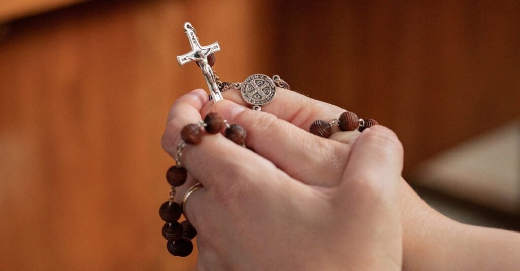 Mãos seguram terço com crucifixo e medalha de São Bento