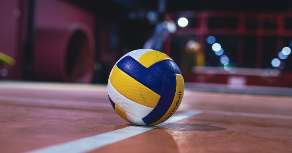 Bola de vôlei azul, amarela e branca sobre quadra indoor