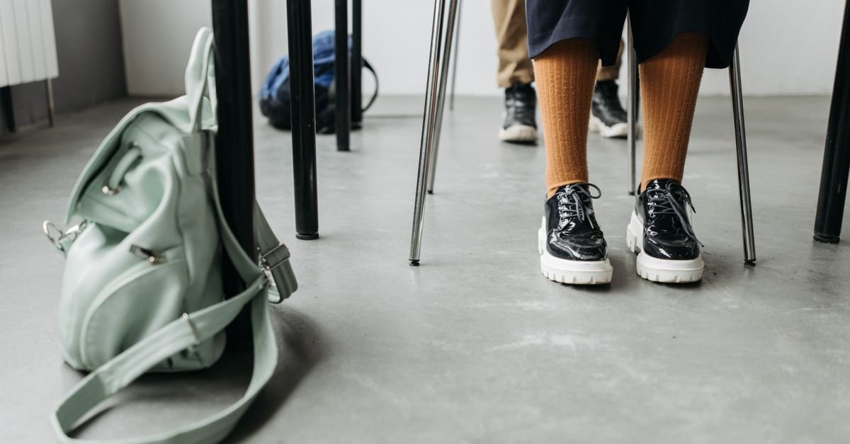 Mochila escolar no chao ao lado de carteira e pes de estudantes em sala de aula