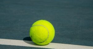 Bola de tenis amarela sobre a linha branca de uma quadra