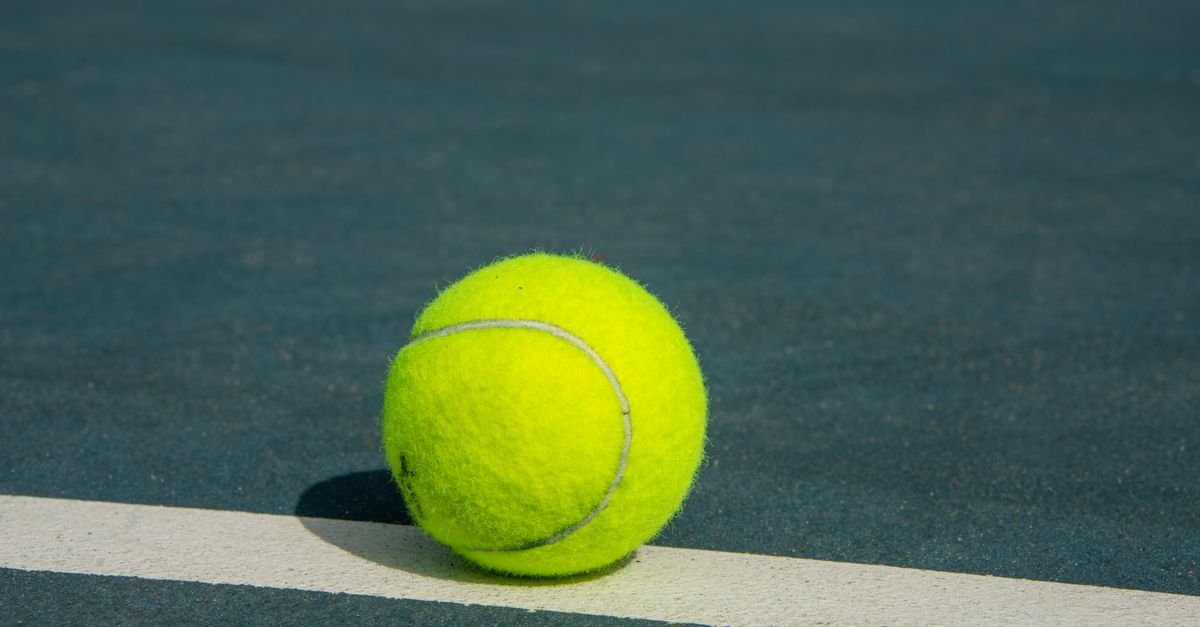 Bola de tenis amarela sobre a linha branca de uma quadra