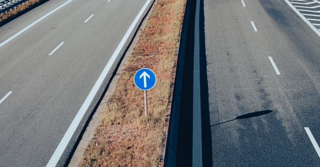 Vista aérea de rodovia de pista dupla com faixas brancas e placa azul de sinalização no canteiro central