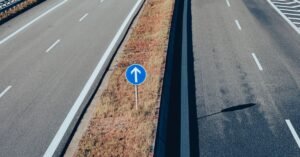 Vista aérea de rodovia de pista dupla com faixas brancas e placa azul de sinalização no canteiro central
