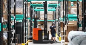 Trabalhadores e empilhadeira em corredor de galpão logístico com prateleiras