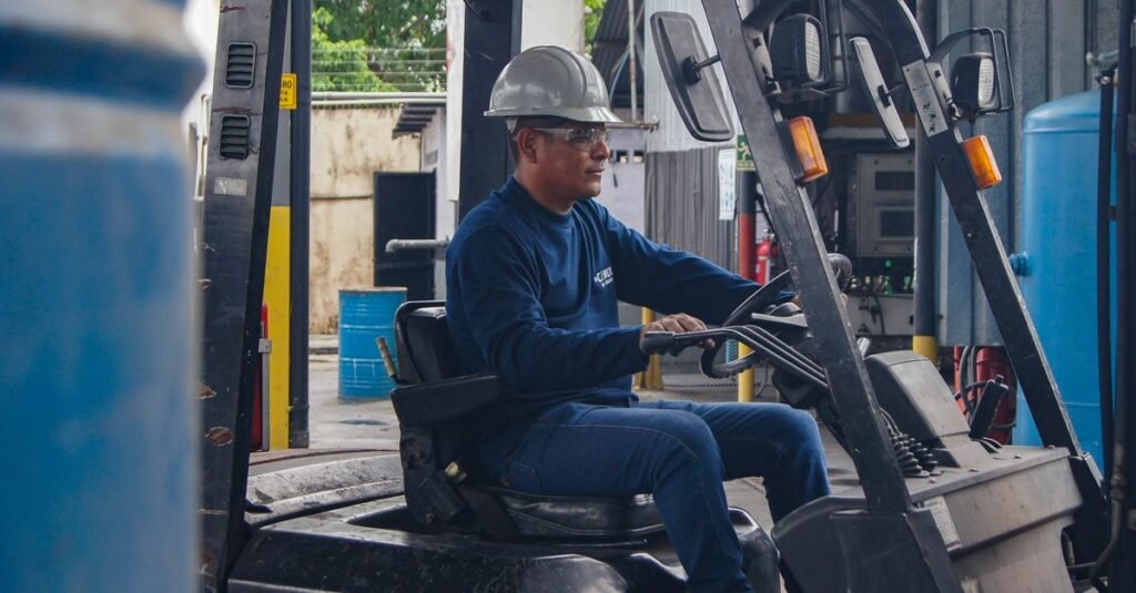 Operador de empilhadeira com capacete e óculos de proteção conduz o equipamento em galpão industrial