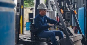 Operador de empilhadeira com capacete e óculos de proteção conduz o equipamento em galpão industrial
