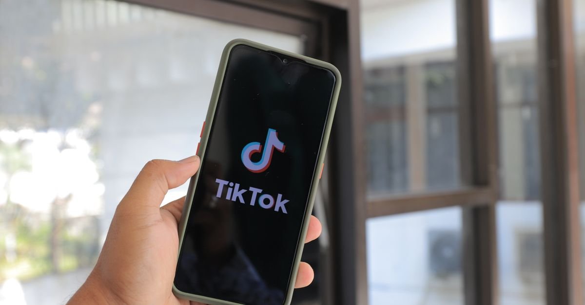 Mão segura celular com a tela de abertura do aplicativo TikTok