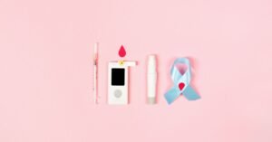 Seringa, medidor de glicemia, lancetador e laço azul sobre fundo rosa, itens usados no controle do diabetes
