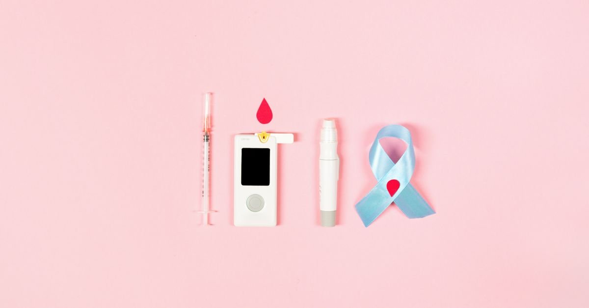 Seringa, medidor de glicemia, lancetador e laço azul sobre fundo rosa, itens usados no controle do diabetes