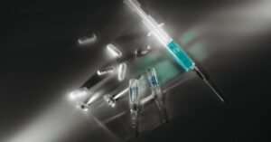 Seringa e cápsulas de medicamento sobre superfície escura, em imagem ilustrativa