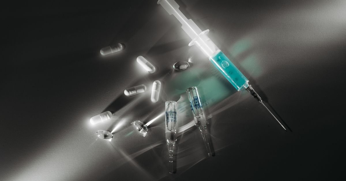 Seringa e cápsulas de medicamento sobre superfície escura, em imagem ilustrativa