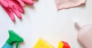 Luvas de borracha, pano, esponjas e frascos de produto de limpeza sobre superfície branca