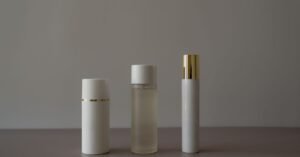 Três frascos brancos de cosmético sem rótulo enfileirados sobre fundo neutro
