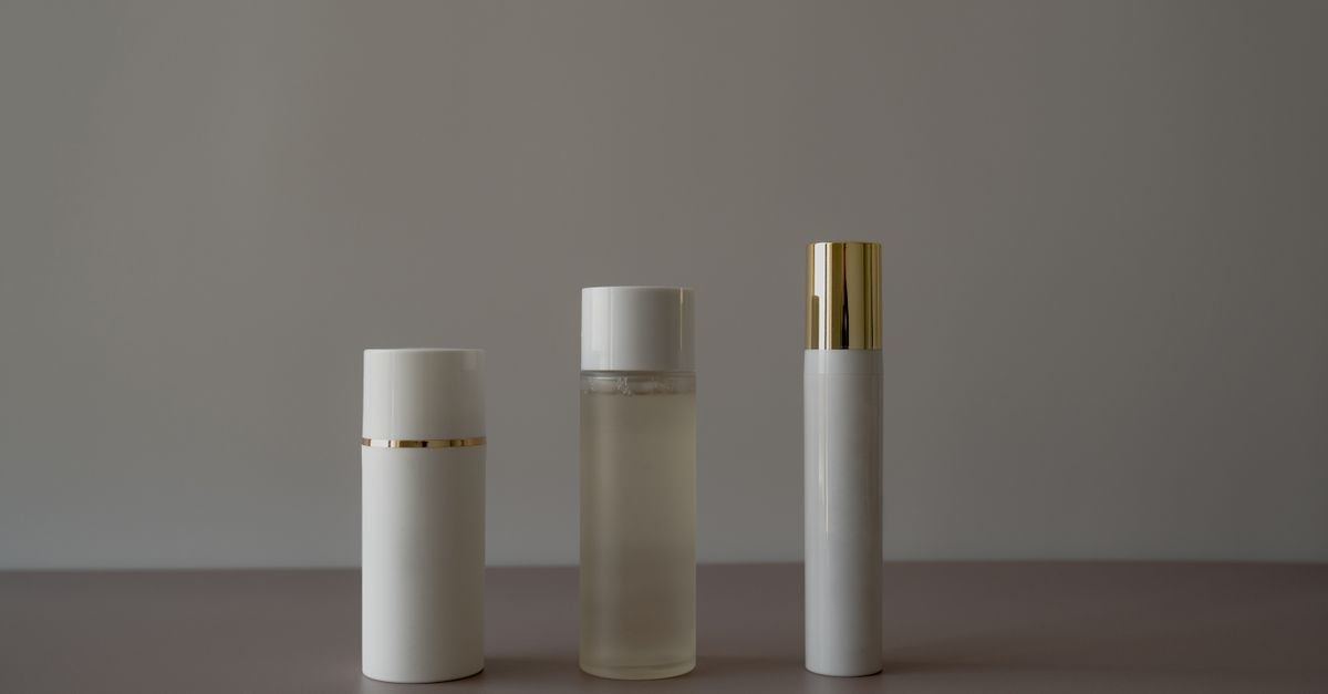 Três frascos brancos de cosmético sem rótulo enfileirados sobre fundo neutro