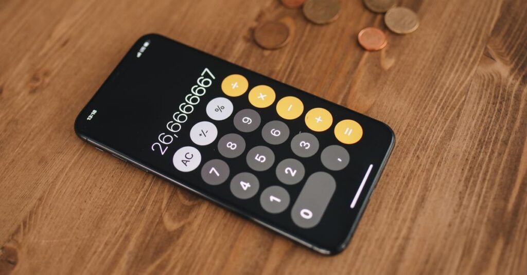 Calculadora em tela de celular sobre mesa de madeira ao lado de moedas