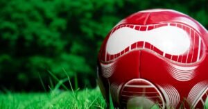 Bola de futebol vermelha e branca sobre a grama de um campo
