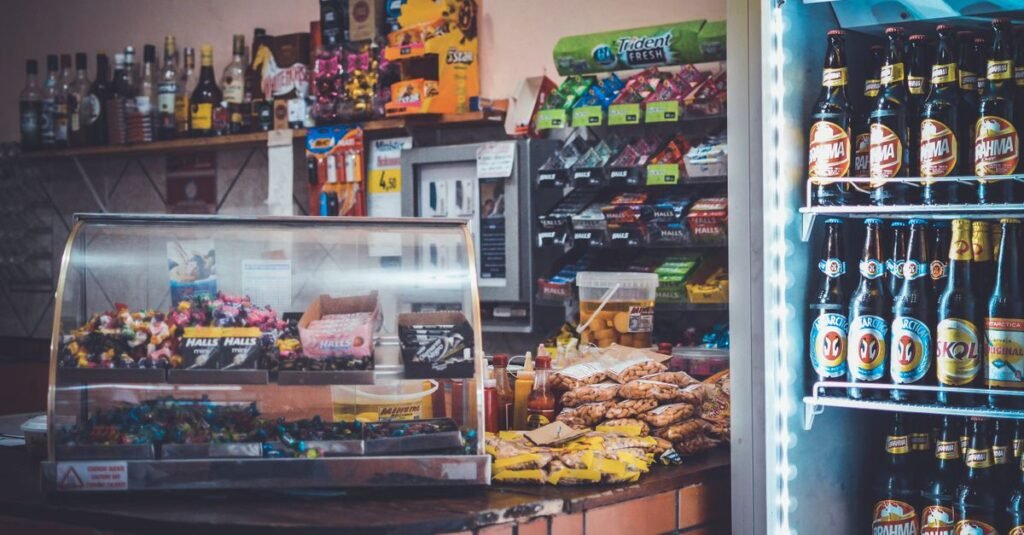Balcão de loja de conveniência com doces, salgados e geladeira de bebidas ao fundo