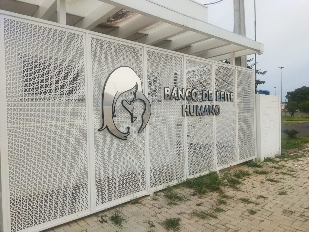 Fachada branca de uma unidade de banco de leite humano com letreiro e logotipo de mãe amamentando