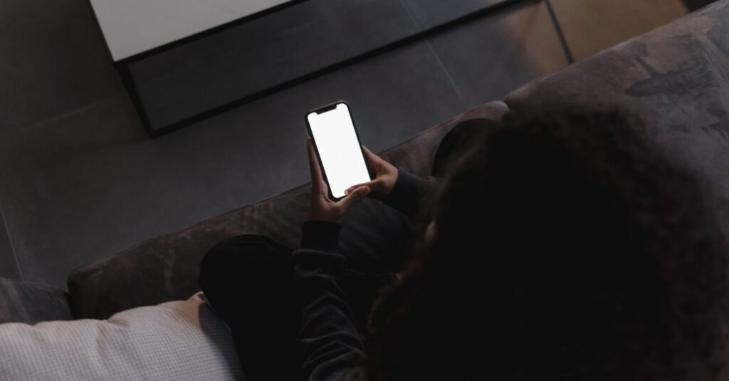 Pessoa sentada no sofa segurando celular com a tela acesa
