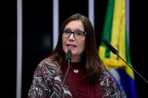 Deputada Bia Kicis discursa em tribuna com a bandeira do Brasil ao fundo