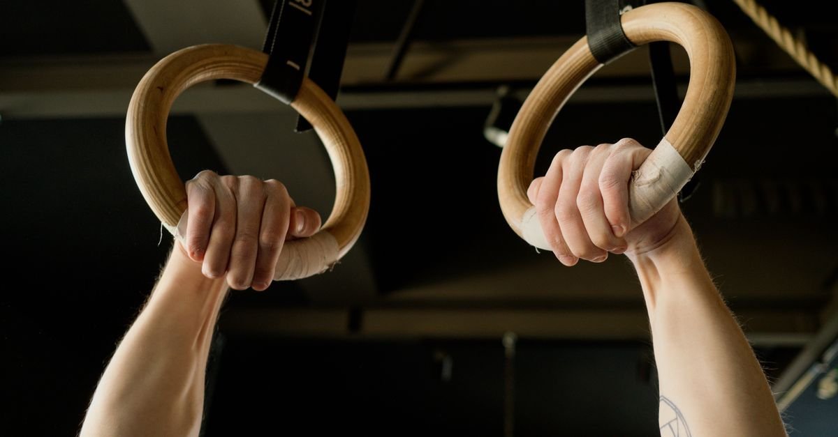 Mãos de atleta segurando argolas de ginástica artística em ginásio