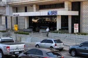 Fachada do edifício sede do BRB, com o logotipo do banco sobre a entrada e carros estacionados em frente