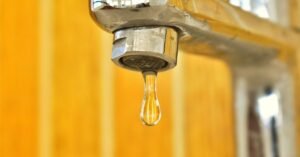 Torneira metálica com uma gota de água prestes a cair