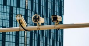 Três câmeras de vigilância montadas em um poste, com prédio ao fundo
