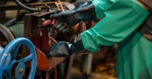 Trabalhador com luvas de borracha e avental de protecao verde operando valvula de equipamento industrial