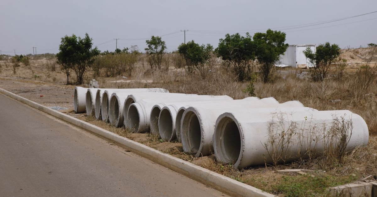 Manilhas de concreto para rede de esgoto alinhadas na margem de uma via em área de cerrado