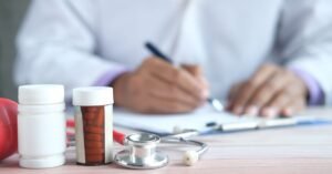 Médico escreve receita sobre mesa com estetoscópio e frascos de remédio
