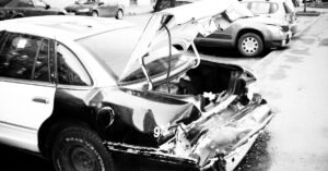 Carro com a traseira destruída após colisão, estacionado em via urbana