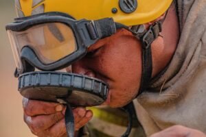 Brigadista com capacete e óculos de proteção bebe água durante combate a incêndio em vegetação