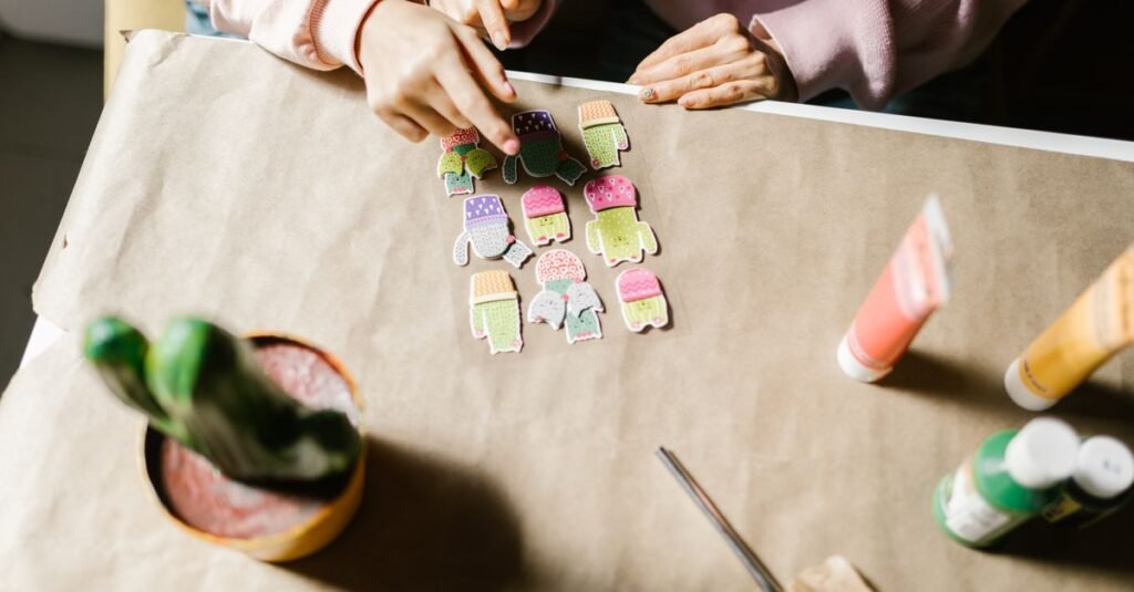 Mãos organizando recortes de papel coloridos sobre uma mesa forrada de papel pardo em oficina de arte