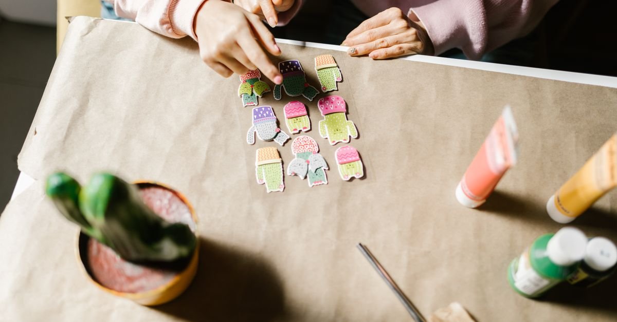 Mãos organizando recortes de papel coloridos sobre uma mesa forrada de papel pardo em oficina de arte