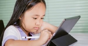 Criança concentrada usando caneta digital em um tablet apoiado sobre a mesa