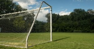 Gol de futebol com rede branca em campo gramado, visto de perto