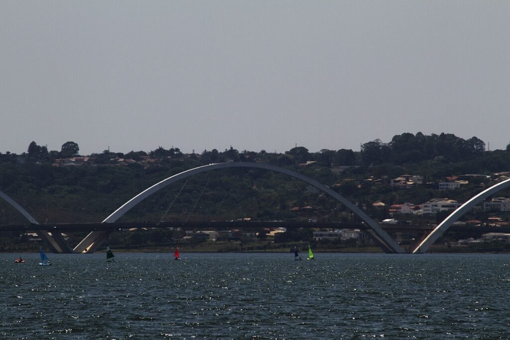 Ponte Juscelino Kubitschek vista do Lago Paranoá, com veleiros na água e os arcos de concreto ao fundo