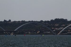Ponte Juscelino Kubitschek vista do Lago Paranoá, com veleiros na água e os arcos de concreto ao fundo
