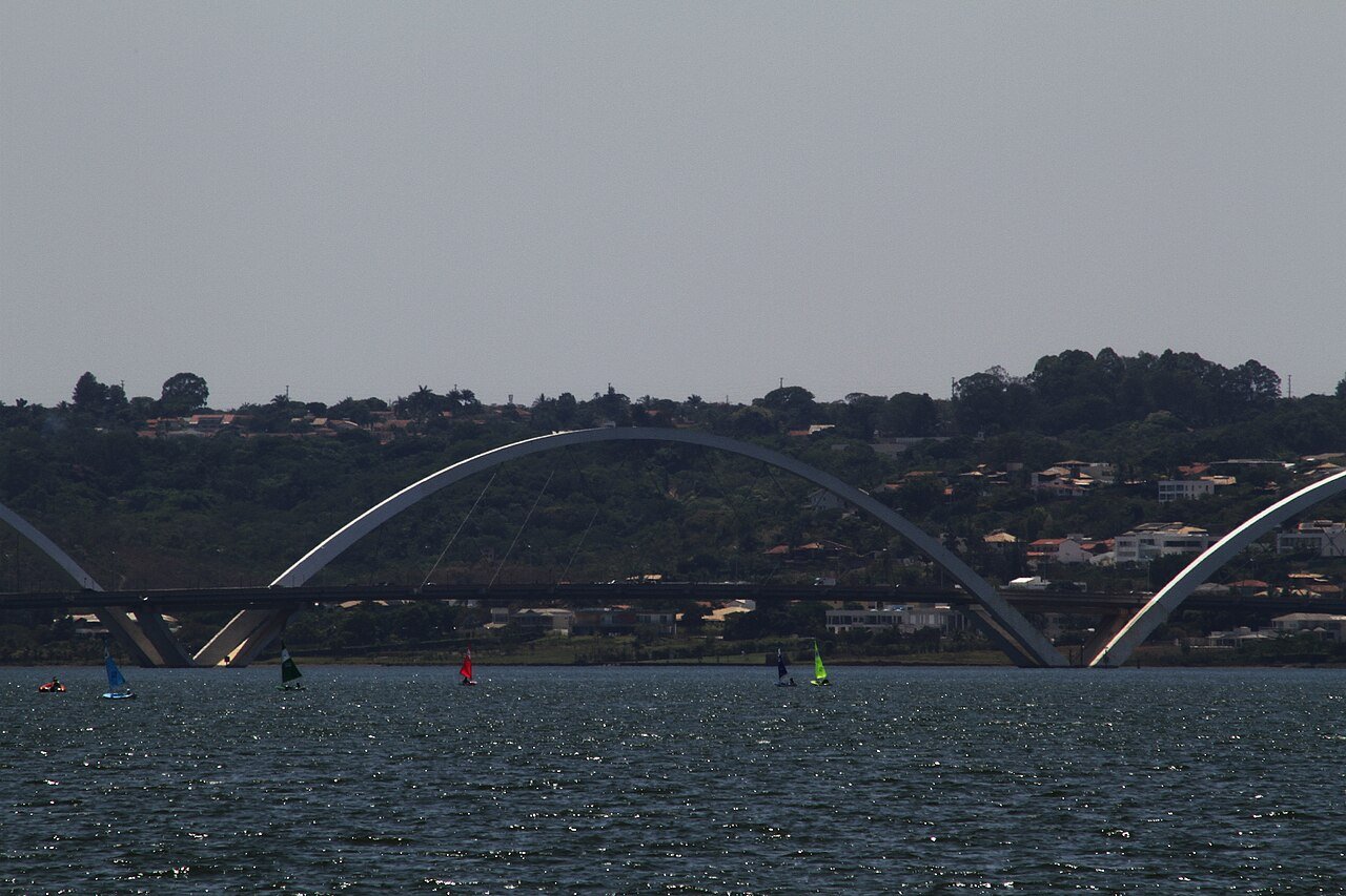 Ponte Juscelino Kubitschek vista do Lago Paranoá, com veleiros na água e os arcos de concreto ao fundo