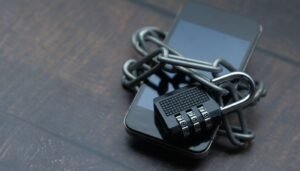 Celular preto sobre mesa de madeira, envolto por uma corrente com cadeado de segredo
