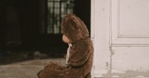 Urso de pelúcia sentado sozinho ao lado de uma porta, em imagem ilustrativa sobre proteção à infância