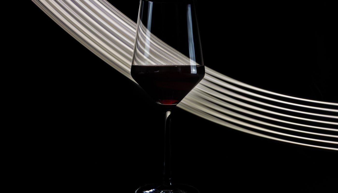 Taça de vinho tinto sobre fundo escuro com faixa de luz