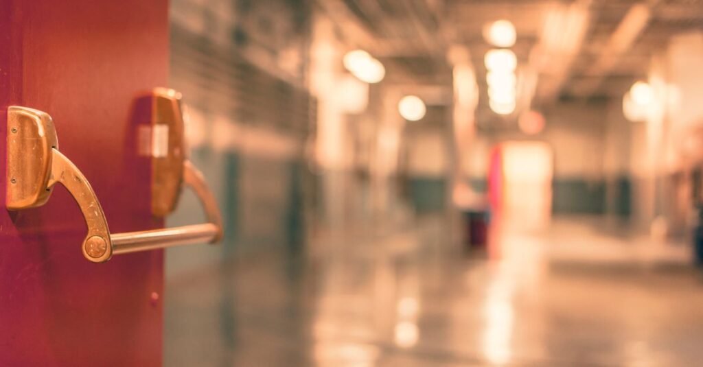 Corredor de escola com porta corta-fogo em primeiro plano e piso refletindo a luz